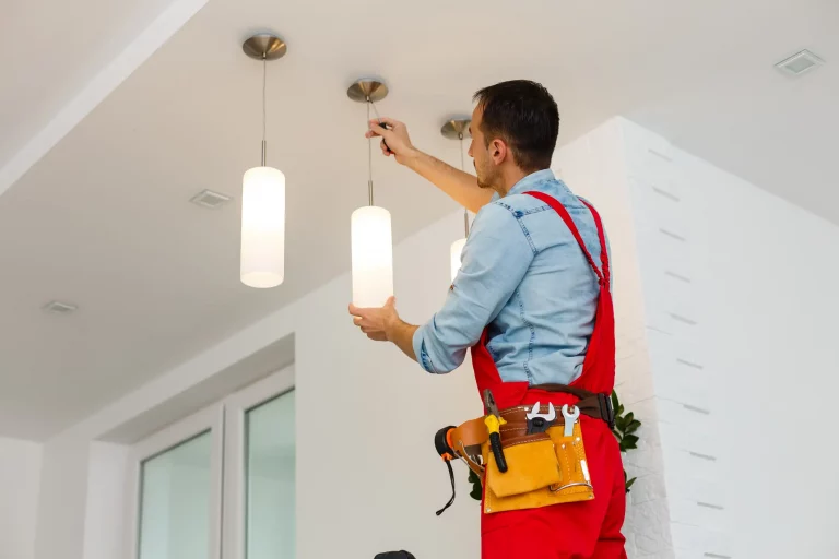 Elektriker in roter Arbeitshose montiert hängende Lampen an einer Decke in einer Wohnung