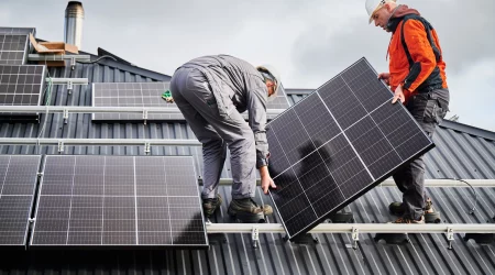 Techniker, die ein Photovoltaik-Solarmodul tragen, während sie eine Solaranlage auf dem Dach des Hauses installieren