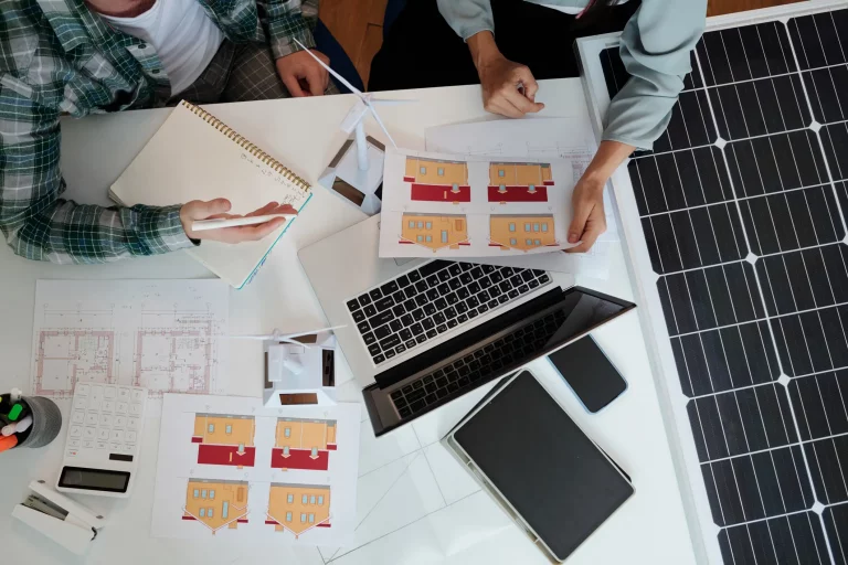 Solarexperte mit Laptop und Unterlagen zu einem Haus auf einem Tisch, gemeinsam mit einem Kunden bei einer Solarberatung