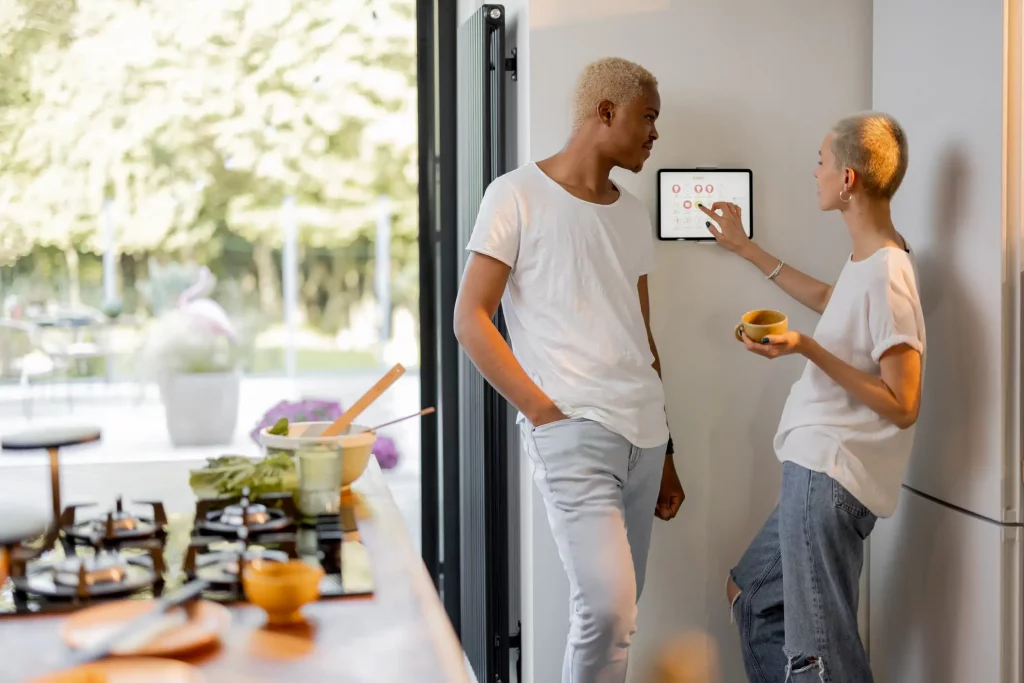 Junge Frau reguliert mit ihrem Partner an einem Smart Home Thermostat einer Wärmepumpe die Temperatur der Wohnung