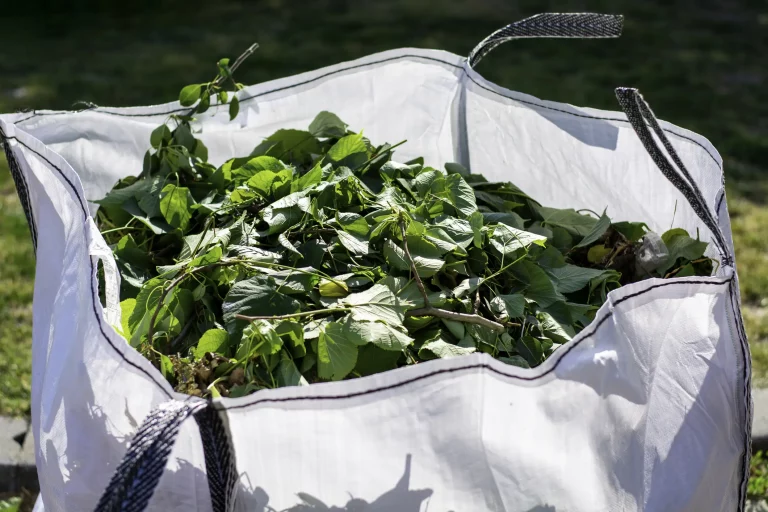 Große weiße Plastiktasche mit Grünschnitt und Gartenabfällen zur Entsorgung