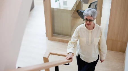 Ältere Dame hält sich am Treppengeländer fest während sie die Treppen steigt