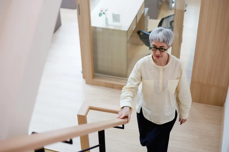 Ältere Dame hält sich am Treppengeländer fest während sie die Treppen steigt