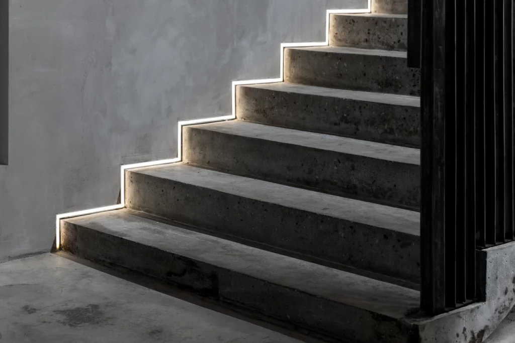 Moderne Treppe aus Sichtbeton mit integrierter LED-Streifenbeleuchtung entlang der Stufenkanten, die für Sicherheit und atmosphärisches Licht sorgt.
