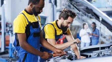 Zwei Werkstattmitarbeiter stehen am Motorblock eines Autos und wechseln die Bremsflüssigkeit
