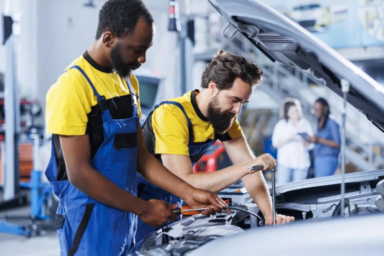 Zwei Werkstattmitarbeiter stehen am Motorblock eines Autos und wechseln die Bremsflüssigkeit