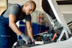 Automechaniker in Arbeitskleidung wechselt ein defektes Teil im Motorraum eines Autos