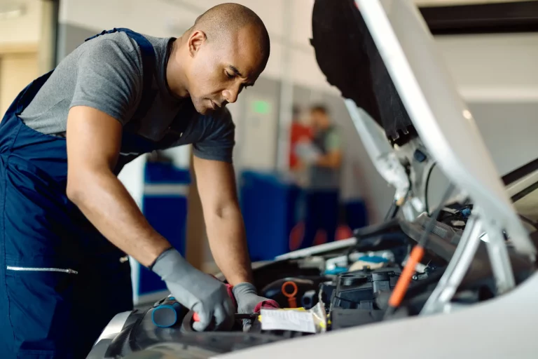 Automechaniker in Arbeitskleidung wechselt ein defektes Teil im Motorraum eines Autos