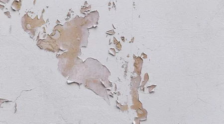 Nahaufnahme einer schlecht reparierten Gebäudefassade, die mit Rissen in Putz und Farbe bedeckt ist