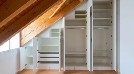 Eine Innenansicht eines maßgefertigten Einbauschranks mit offenen Türen, die in ein Schlafzimmer mit Dachschräge eingebaut sind