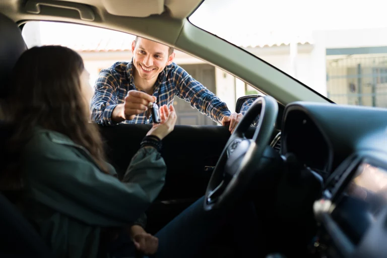 Vater gibt seiner Tochter die im Auto sitzt den Autoschlüssel