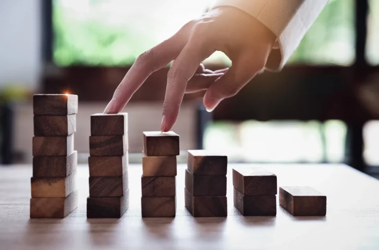 Zwei Finger eines Finanzberaters die auf unterschiedlich hohe Holzstapel gelegt sind als Symbolik eines Sparplans