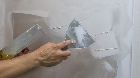 Maler bringt Spachtelputz mit einer Spachtel an einer Trockenbauwand im Innenbereich an
