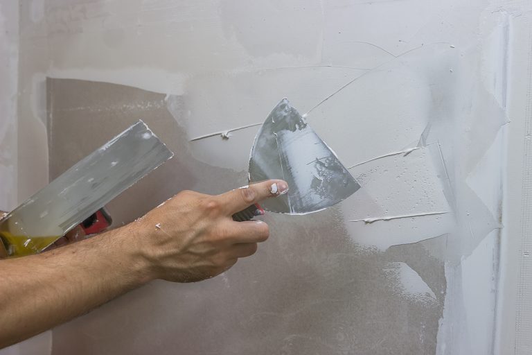 Maler bringt Spachtelputz mit einer Spachtel an einer Trockenbauwand im Innenbereich an