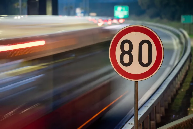 Verkehrszeichen mit 80 km/h Höchstgeschwindigkeit auf der Autobahn mit Autos im Hintergrund in voller Bewegung