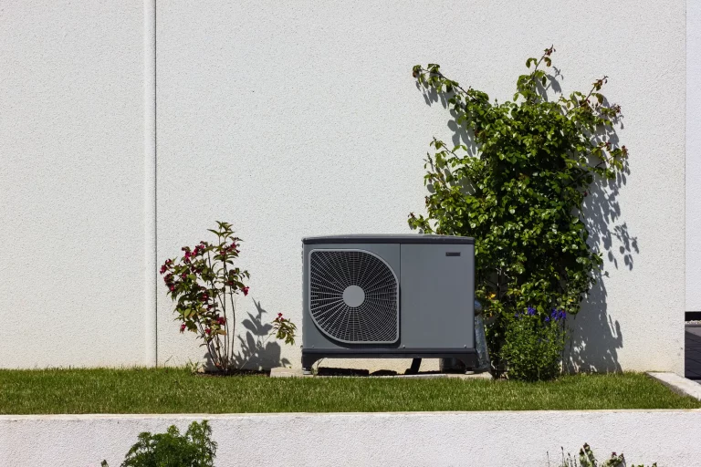 Wärmepumpe auf einer grünen Wiese in einem Garten vor einer Hauswand