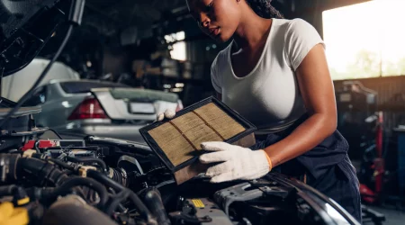 Automechanikerin mit weißen Handschuhen arbeitet im Motorraum eines PKWs und ersetzt einen Filter