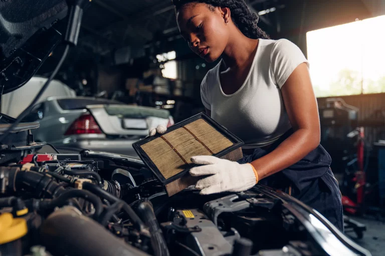 Automechanikerin mit weißen Handschuhen arbeitet im Motorraum eines PKWs und ersetzt einen Filter