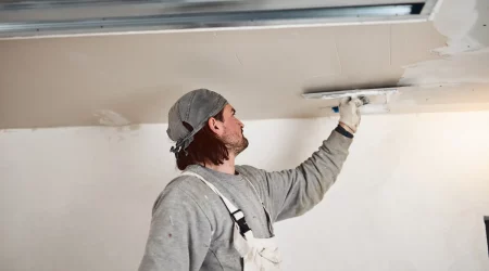 Maler verputzt mit einer Kelle eine Trockenbaudecke in einem Raum