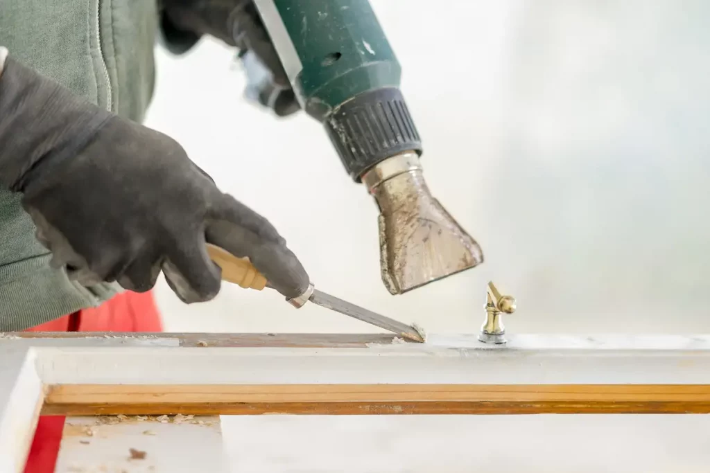 Restaurator entfernt mit einem Heißluftföhn und Spachtel Lack von einem alten Fensterrahmen