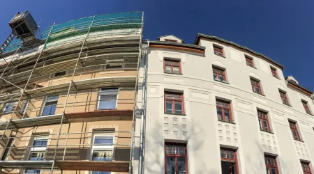 Zwei nebeneinander stehende Gebäude mit vorher und nachher Effekt einer Fassadensanierung. Das Haus links mit Gerüst vor der Sanierung der Fassade. Das Haus rechts mit fertig sanierter Fassade.