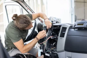 Kfz-Mechatroniker arbeitet in einer Werkstatt an der Elektronik eines Autos im Fahrerraum