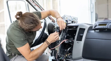 Kfz-Mechatroniker arbeitet in einer Werkstatt an der Elektronik eines Autos im Fahrerraum