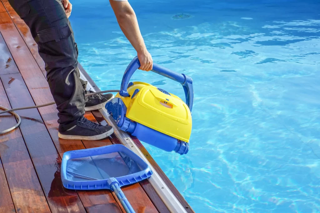 Ein Mann hält einen Roboter zur Poolreinigung in der Hand und lässt diesen ins Wasser.