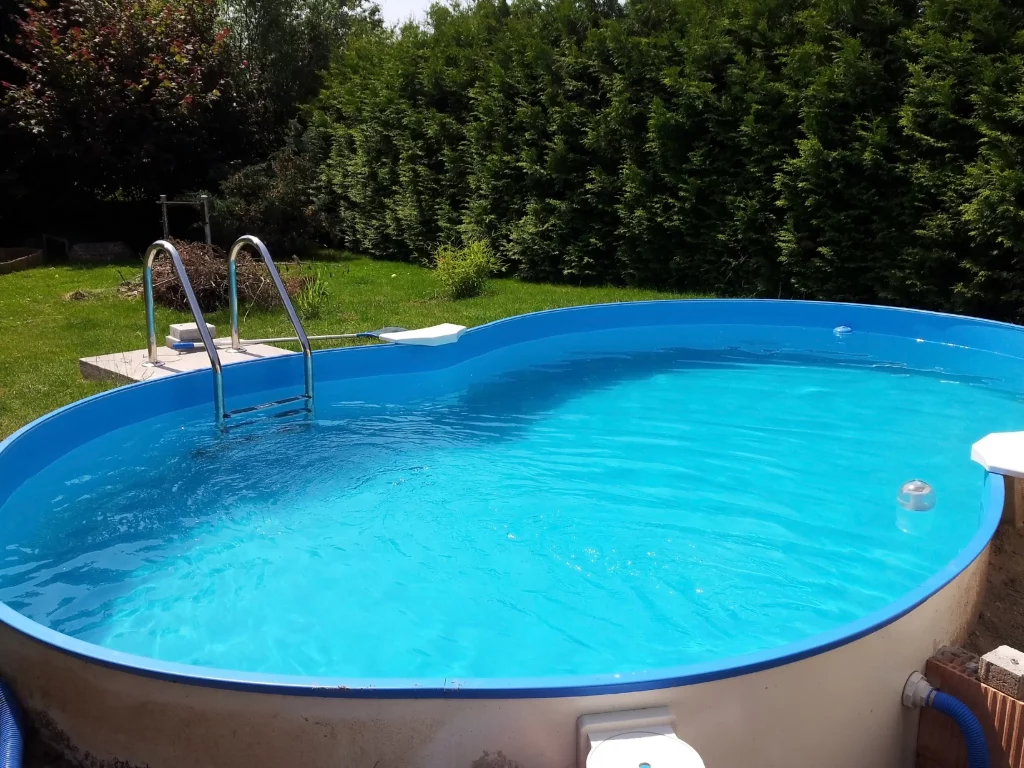 Ein ovaler, achtförmiger Stahlwandpool mit Pumpe und einer Metallleiter in einem Garten.