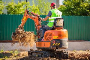 Baggerfahrer auf einem orangenen Minibagger in einem Garten mit Erde in der Schaufel