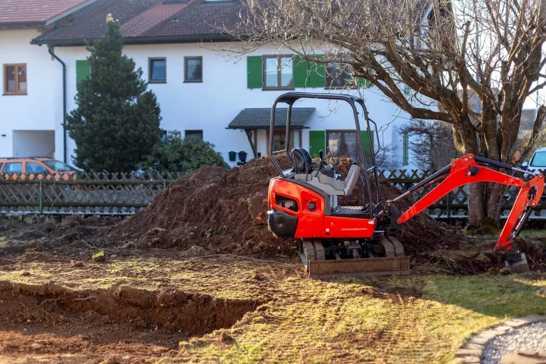 Ein kleiner roter Minibagger in einem Garten vor einer angefangenen Grube