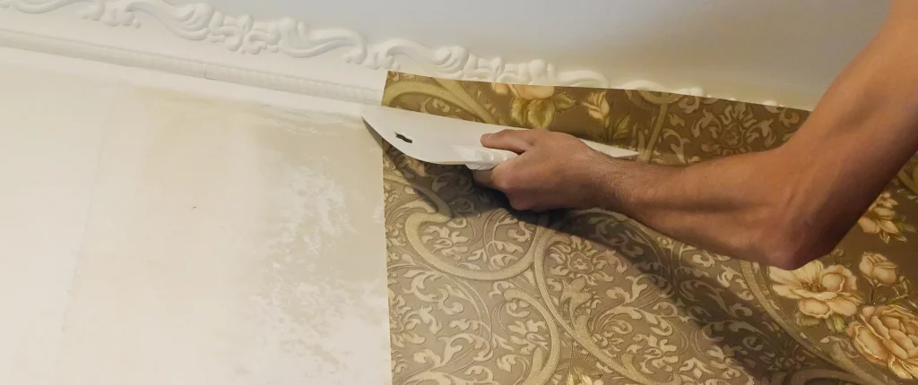 Tapezierer bringt mit einer großen Tapezierspachtel eine goldene Prägetapete an einer Wand an