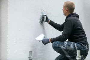 Ein Verputzer bringt mit einer Kelle Reibeputz an einer Wand an