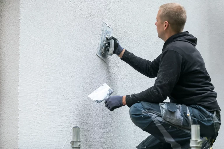 Ein Verputzer bringt mit einer Kelle Reibeputz an einer Wand an