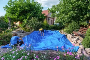 Eine blaue Teichfolie wird in einem Aushub für einen Gartenteich ausgelegt