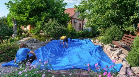 Eine blaue Teichfolie wird in einem Aushub für einen Gartenteich ausgelegt