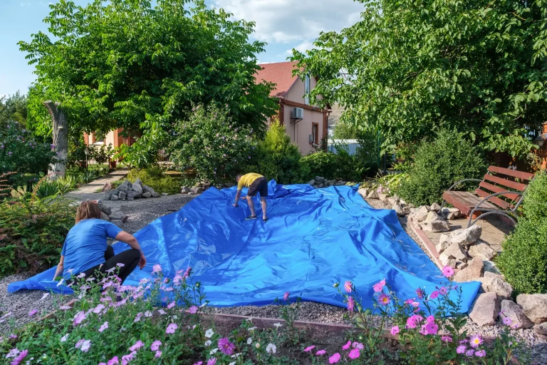 Eine blaue Teichfolie wird in einem Aushub für einen Gartenteich ausgelegt