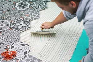 Fliesenleger trägt bei der Fliesenverlegung mit einer Kelle Fliesenkleber auf den Boden auf