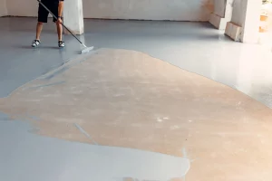 Estrichleger beim Auftragen von Epoxidharz in einer Industriehalle zur Versiegelung von Estrich