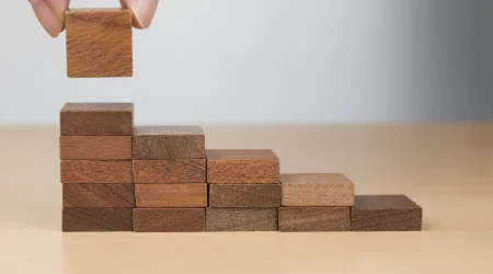 Eine Frauenhand stapelt Holzklötze zu einer Treppe