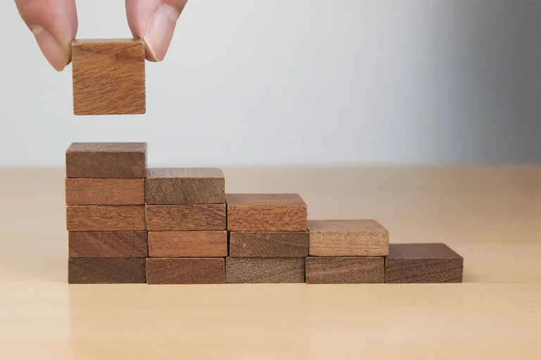 Eine Frauenhand stapelt Holzklötze zu einer Treppe