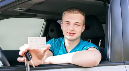 Junge in blauem T-Shirt hält seinen Führerschein in der Hand