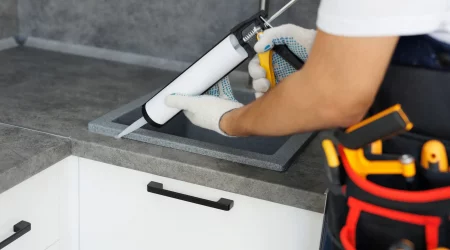 Küchenbauer verfugt das Waschbecken bei einer neu eingebauten Küchenarbeitsplatte mit einer Silikonpistole