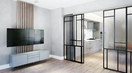Modernes Wohnzimmer mit maßgefertigten Glastüren, die Küche und Wohnbereich trennen. Die Glastüren haben schwarze Metallrahmen und geriffelte Glasflächen. Der Raum ist minimalistisch gestaltet mit einem großen Flachbildfernseher an einer Akzentwand und einem eleganten, schwebenden Sideboard. Heller Holzboden und dezente Beleuchtung sorgen für eine einladende Atmosphäre.