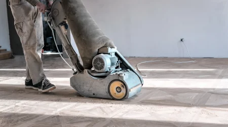 Ein Bodenleger schleift mit einer professionellen Schleifmaschine einen Parkettboden ab