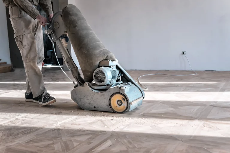 Ein Bodenleger schleift mit einer professionellen Schleifmaschine einen Parkettboden ab