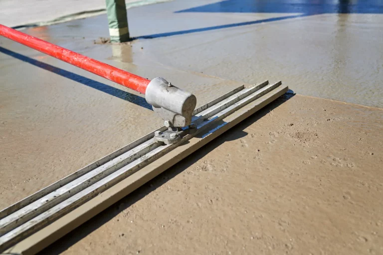 Nahaufnahme eines Werkzeugs zur Glättung von schwimmendem Estrich auf einer Baustelle. Das rote Werkzeug wird verwendet, um eine ebene und glatte Oberfläche auf dem frisch gegossenen Estrich zu erzeugen. Schwimmender Estrich verbessert die Stabilität und den Schallschutz von Fußböden.