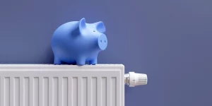 blaues Sparschwein auf einem Heizkörper, der an einer blauen Wand hängt