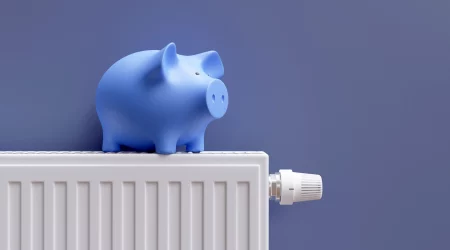 blaues Sparschwein auf einem Heizkörper, der an einer blauen Wand hängt