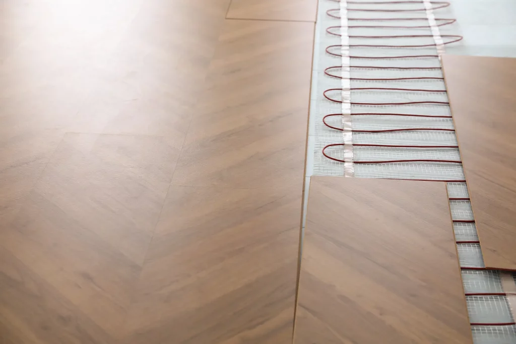 Installation von Laminatboden mit Fußbodenheizung: Detailaufnahme zeigt den Prozess der Verlegung von Laminatdielen über Heizkabeln, die auf einem Netz montiert sind.